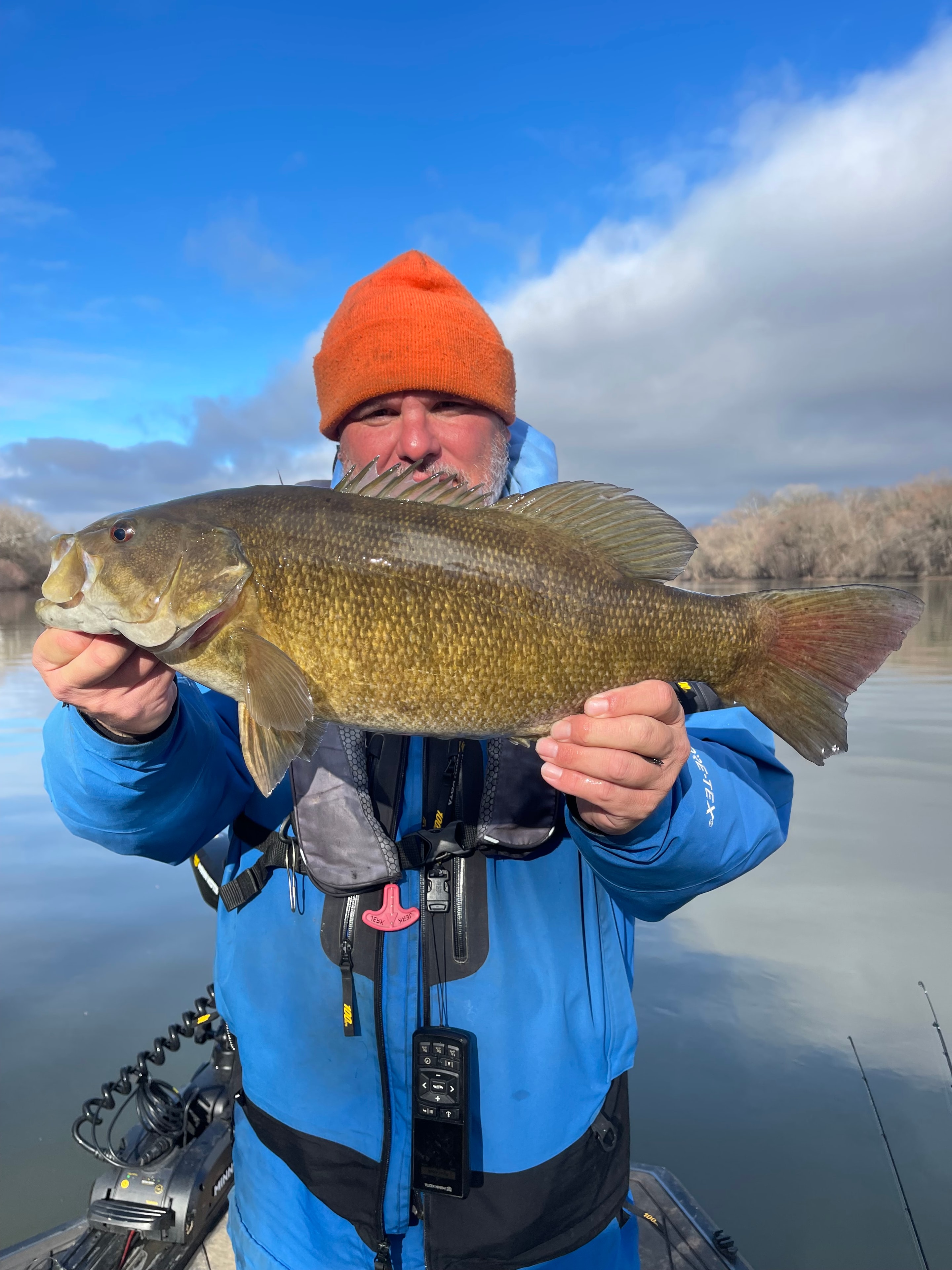 Smiling angler holding a trophy smallmouth bass on the river on a sunny day